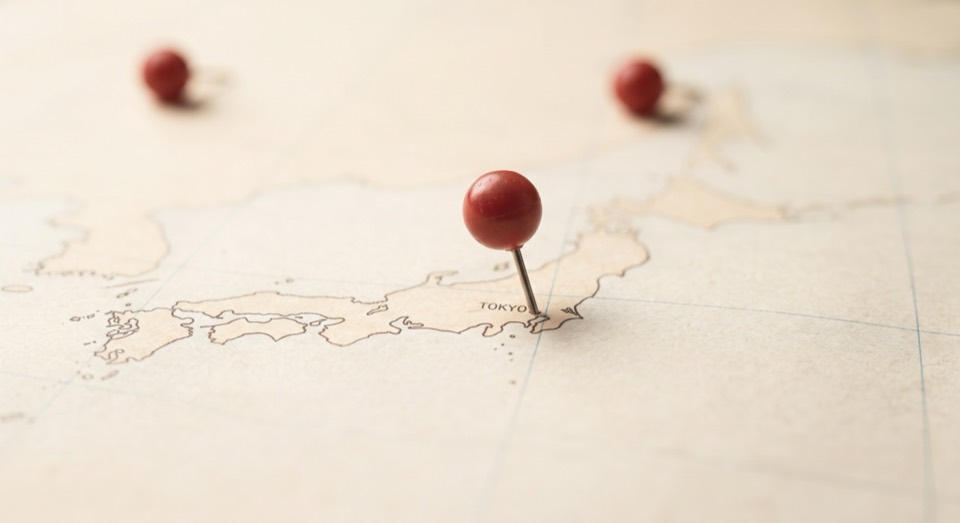 A red map pin marking Tokyo on a paper map